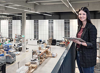 Mitarbeiterin von Streit Service & Solution steht im modernen Logistikzentrum und arbeitet an einem Tablet. Im Hintergrund ist die Autostore Anlage zu sehen.