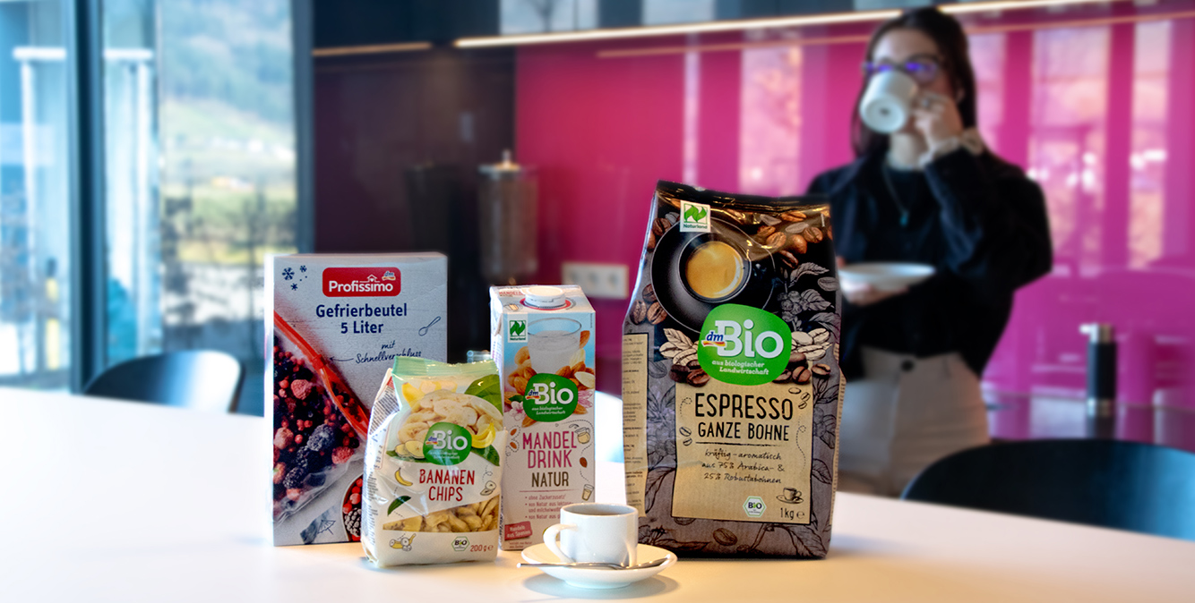Produkte von dem stehen auf einem Tisch. Im Hintergrund trinkt eine Frau Kaffee